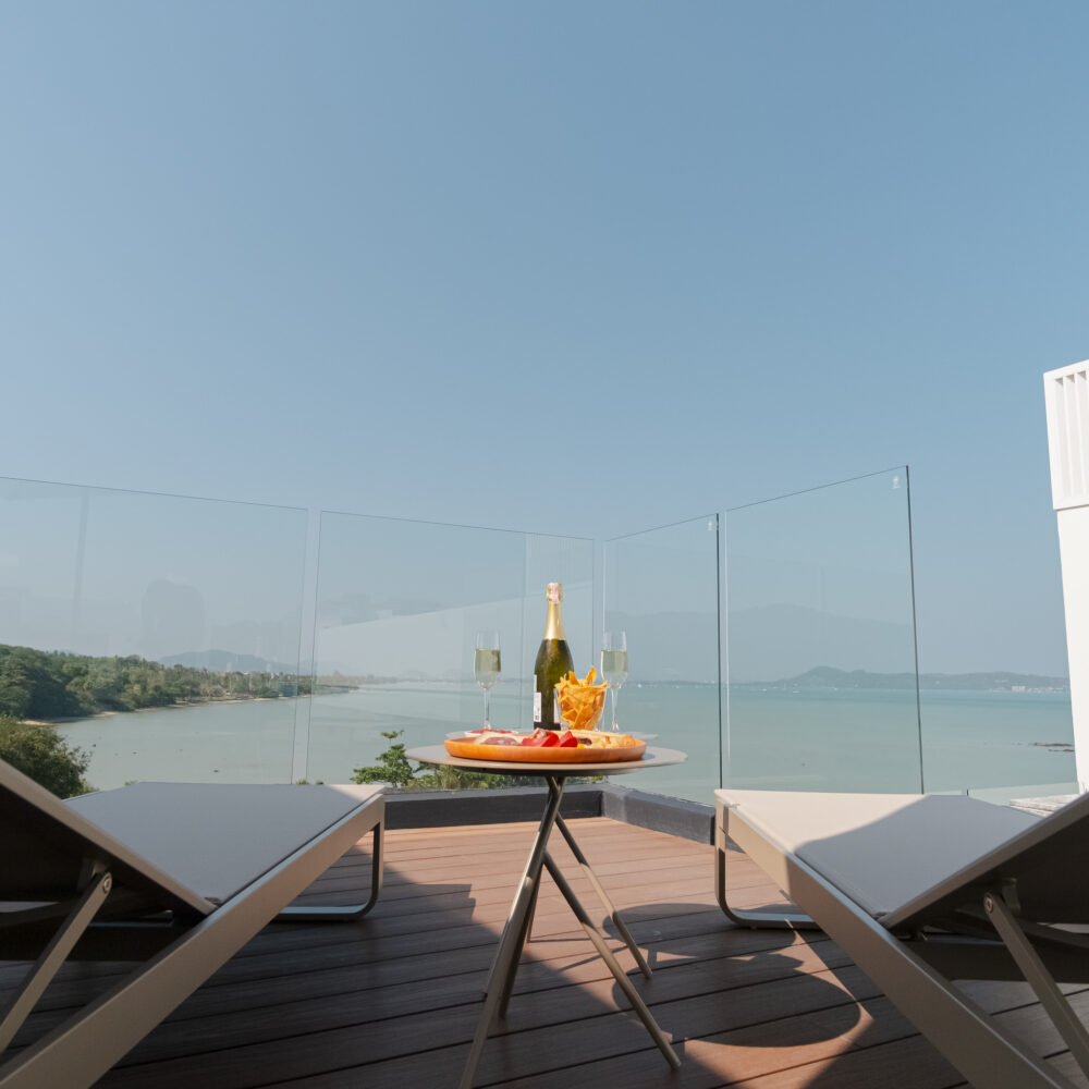 Seaview rooftop terrace with sun loungers, champagne bottle, and cold cuts overlooking Chalong bay