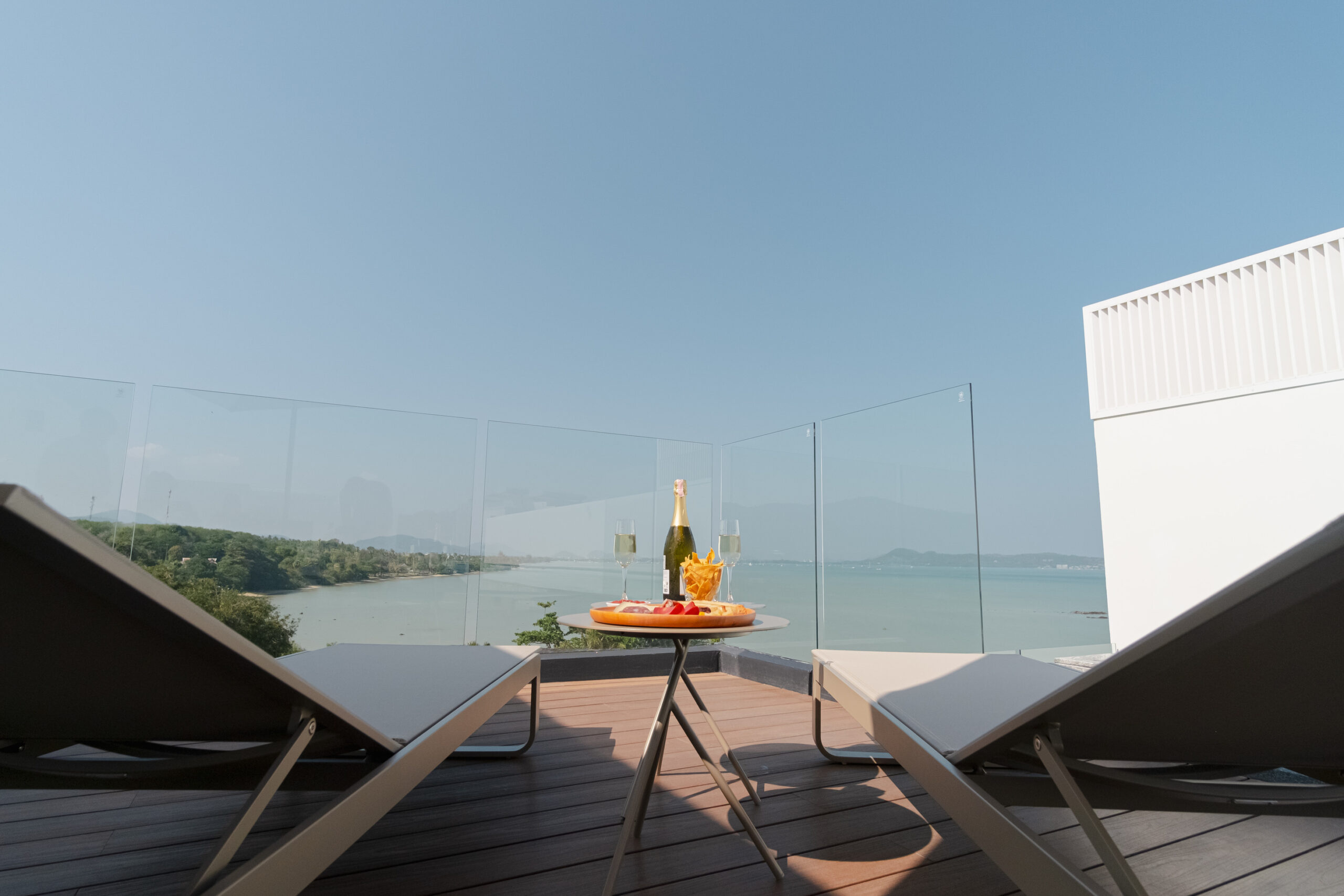 Seaview rooftop terrace with sun loungers, champagne bottle, and cold cuts overlooking Chalong bay